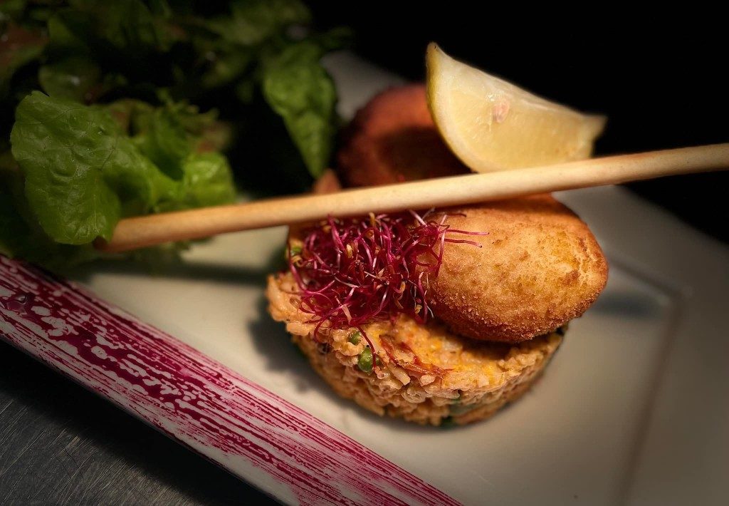 Une croquette dorée avec un bâtonnet de pain, un citron et de la salade, sur une assiette allongée